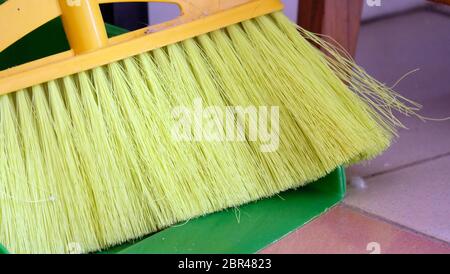 Closeup of yellow plastic broom on a green dustpan. Stock Photo