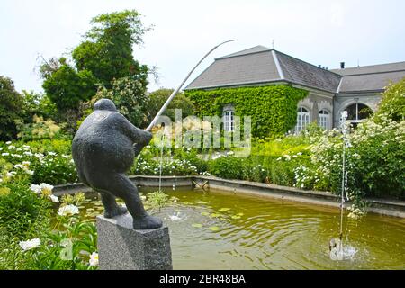Traditional formal public garden, in bloom with a statue fishing in the pond, located near Kvaerndrup, in the south of the island of Funen, Denmark. Stock Photo