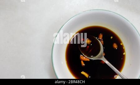 Top view of a bowl of condiment made from soy sauce and raw chili, with a metal teaspoon inside the bowl. Copy space on the left. Stock Photo