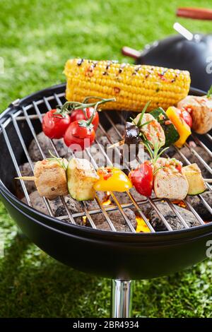 Grilling vegetables and meat kebabs on grid barbecue grill, viewed in close-up on green grass lawn Stock Photo
