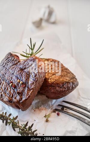 Two prime beef fillet medallions with fresh thyme and rosemary seasoned with black pepper and served on crumpled white paper in a close up presentatio Stock Photo
