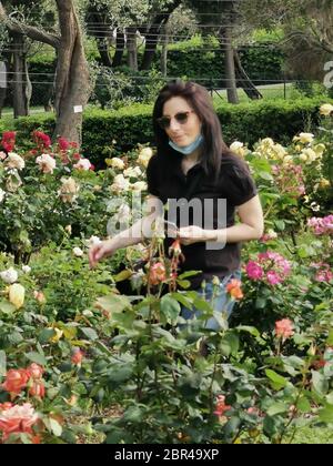 Young woman strolls in a rose garden with mask Stock Photo