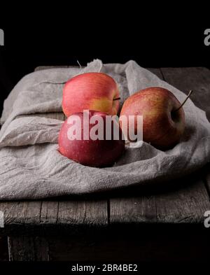 three fresh red apples lay on gray linen napkin, dark background Stock Photo
