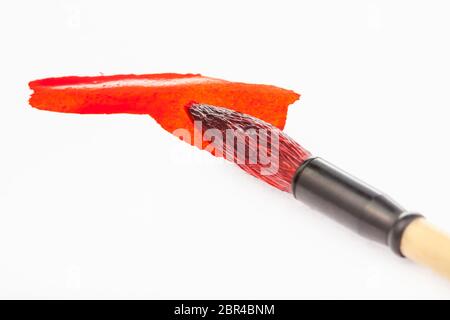red painted round goat hair tip of paintbrush for sumi-e ( suibokuga) painting in red stain on white paper close up Stock Photo