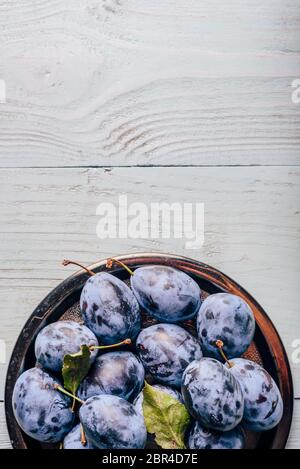 Ripe plums on metal plate over light wooden surface. Copy space Stock Photo