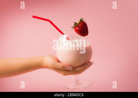 Female hand is holding a delicious healthy strawberry milkshake drink with whipped cream on bright pink background.