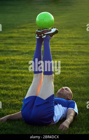 The senior soccer player is practicing soccer practices with soccer ball lying down on lawn outdoors. Stock Photo