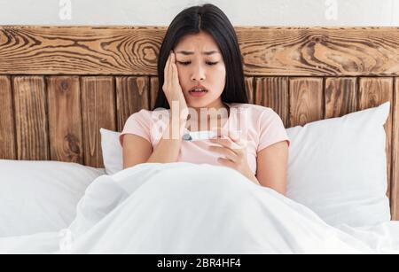 Sick Asian Girl Having Fever Holding Thermometer Sitting In Bed Stock Photo