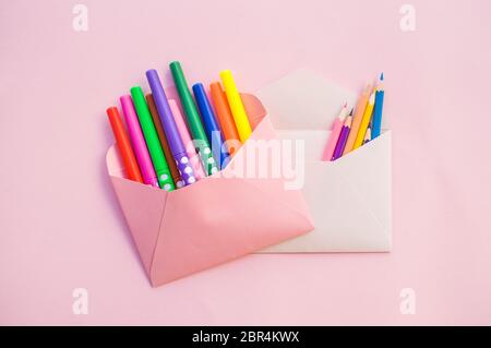 Paper pink and white envelopes full of colorful markers and pecils on pastel pink background with copyspace. Stock Photo