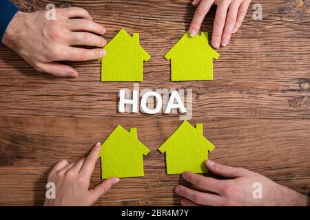 Homeowner Association Text Surrounded By People Holding House Model On Wooden Surface Stock Photo