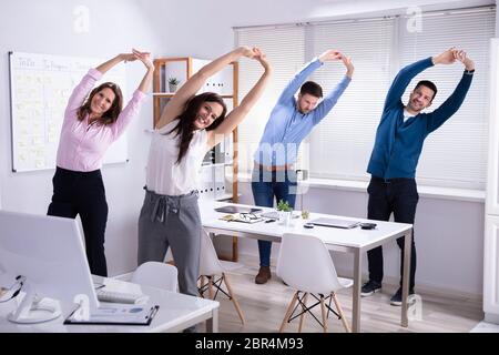 Happy Businesspeople Doing Stretching Exercise Behind Desk At Workplace Stock Photo