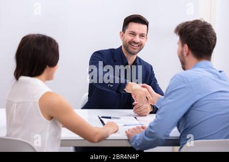 Close-up Of Young Woman Looking At Two Businessmen Shaking Hands In Office Stock Photo