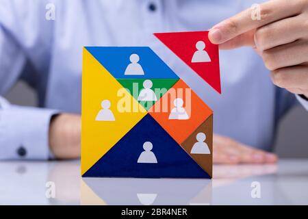 Businessman's Hand Building Tangram Square Block With Human Figures Stock Photo