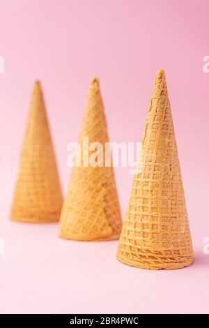 Three upside down wheat flour ice cream cones diagonally towards the bottom on a pink background. Summer concept. Stock Photo