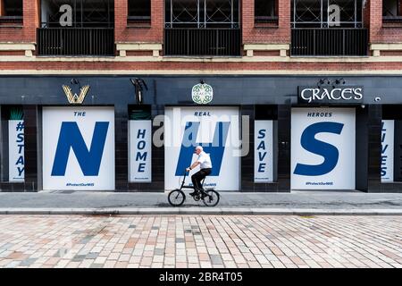 Glasgow, Scotland, UK. 20th May, 2020. Glasgow coronavirus lockdown - an elderly male cyclist passes a giant 'NHS Stay Home Save Lives' sign in the windows of a closed pub in Glasgow city centre Credit: Kay Roxby/Alamy Live News Stock Photo