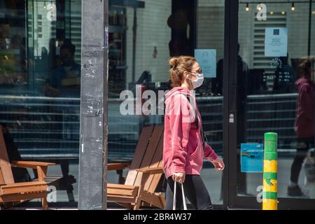 Montreal, CA - 20 May 2020: Woman with face mask for protection from COVID-19 walking down the street Stock Photo