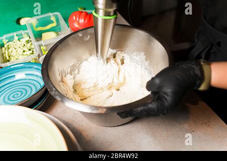 Chef making cheese mix for cheese pancake at restaurant. Blender whips the cottage cheese. Cheesecake preparing. Stock Photo