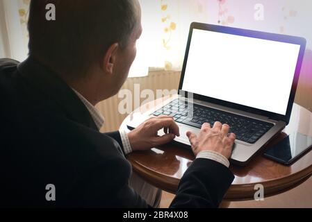 Senior man in smart clothes browsing by using laptop with a phone next to it on a table at home blank screen copy space Stock Photo