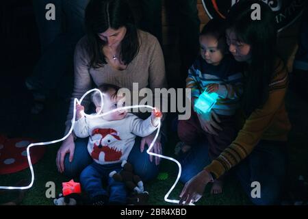 Mother and baby sensory play group are using LED lighting and toys for developmental play. Stock Photo