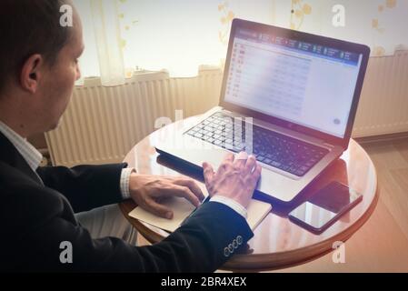 Intelligent expert senior businessman in smart clothes analysing stock market by browsing his laptop and taking notes with pencil Stock Photo