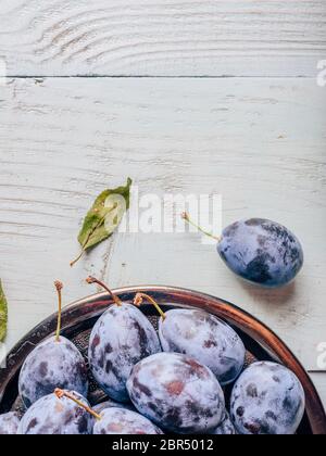 Ripe plums on metal plate over light wooden surface. Copy space Stock Photo