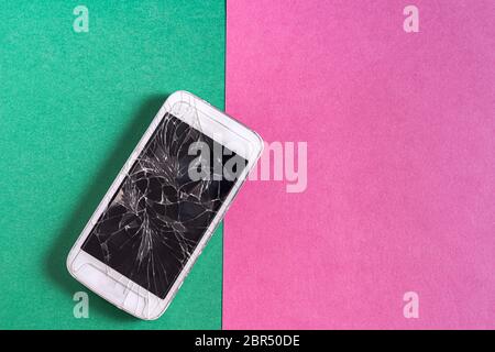 Modern Smartphone with broken screen on colorful paper background. Stock Photo