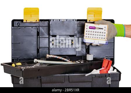 Plumber or carpenter tool box isolated. Black plastic tool kit box with assorted tools and a mans hand with glove holding a screwdriver Bit set. Isola Stock Photo