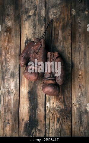 very old leather brown boxing gloves hang on an old shabby wooden wall Stock Photo