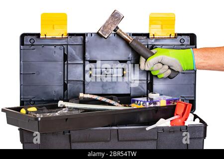 Plumber or carpenter tool box isolated. Black plastic tool kit box with assorted tools and a mans hand with glove holding a hammer made of steel. Isol Stock Photo