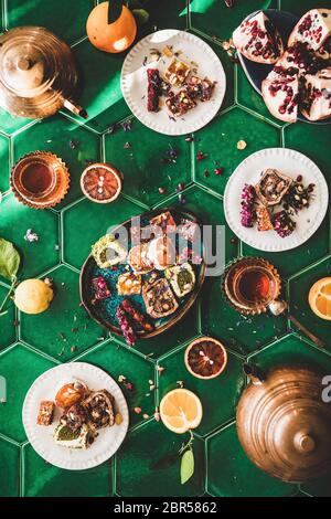 Flat-lay of variety of Turkish traditional lokum sweet delight with Turkish tea in copper pots and tulip glasses over green Moroccan tile table, top v Stock Photo