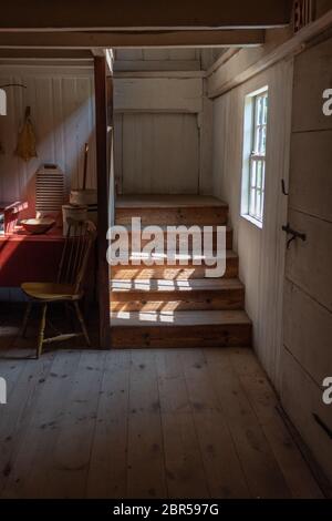 Interior of a very old fishing shack, light streaming through window onto stairs, table and chair, vertical aspect Stock Photo