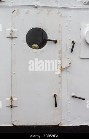 Ship door painted white with round porthole window, chained and padlocked, creative copy space, entry denied, vertical aspect Stock Photo