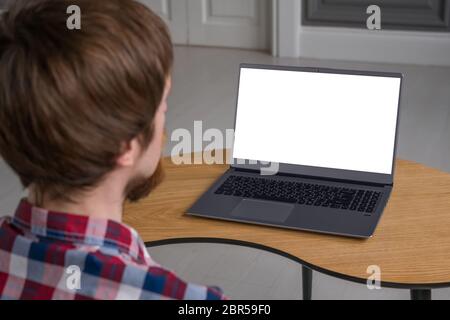 Mockup image of man looking at grey laptop with white blank screen on wooden table in home interior. Mock up, copyspace, freelance workspace, template Stock Photo