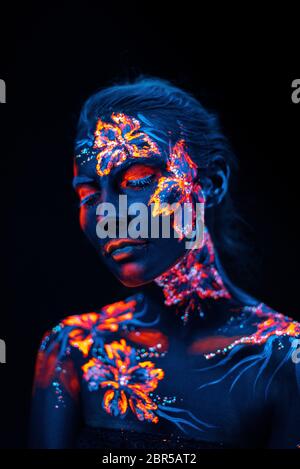 Conceptual face art with shining flowers painted in fluorescent colors isolated on black background Stock Photo