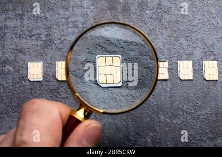 Person's Hand Holding Magnifying Glass Over Nano Sim Card On Rough Background Stock Photo