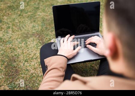Man works at a laptop while sitting on the grass Stock Photo
