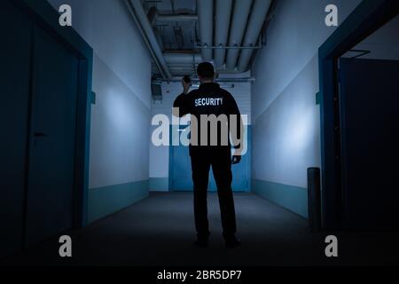 Rear View Of A Male Security Guard With Flashlight Standing In Corridor Stock Photo