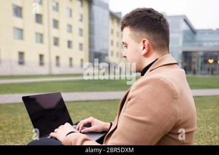 Man works at a laptop while sitting on the grass Stock Photo