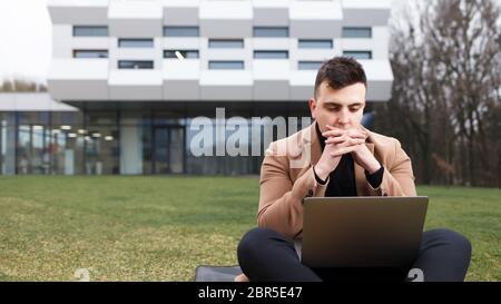 Man concentrated on laptop sitting on grass near university Stock Photo