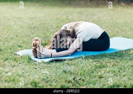 flexible sporty woman doing stretching yoga in park Stock Photo