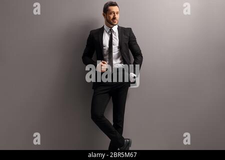 Male model in a black suit leaning on a gray wall Stock Photo
