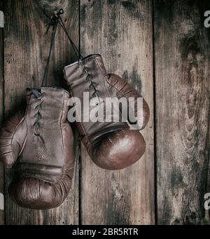 very old leather brown boxing gloves hang on an old shabby wooden wall, sport background Stock Photo