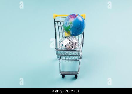 a disco ball and a planet earth in a supermarket shopping cart turquoiseon a turquoise background. Minimal still life color photography Stock Photo