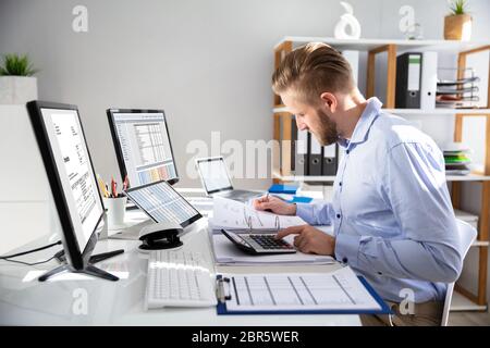 Businessperson Calculating Invoice With Computer On Desk Stock Photo