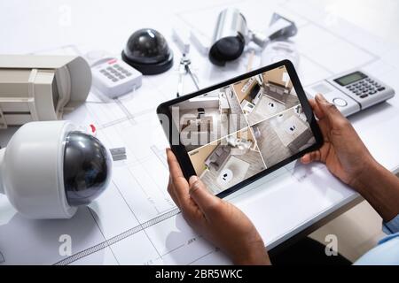 An Elevated View Of Person Watching Footage On Digital Tablet With Security Equipment On Blueprint Stock Photo