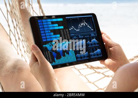 Close-up Of A Woman Lying On Hammock Analyzing The Graph On Digital Tablet At Beach Stock Photo