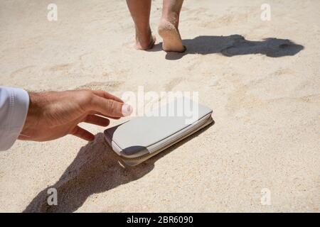 Close-up Of A Man Taking Woman's Lost Purse On Sand At Beach Stock Photo