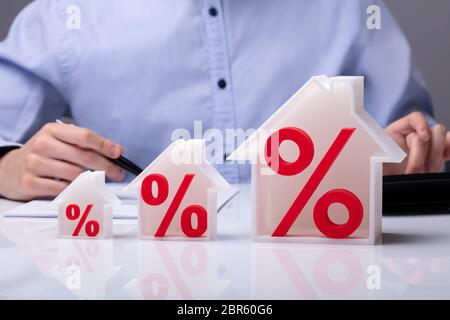 Close-up Of A House Models With Percentage Symbol In Front Of Businessperson Working In Office Stock Photo