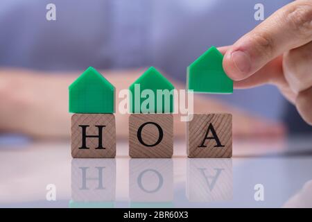 Businessman's Hand Placing House Models On Wooden HOA Cubic Blocks Over Desk Stock Photo