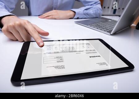 Close-up Of Businessman's Hand Checking Invoice On Tablet Over Desk Stock Photo